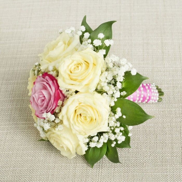 Presented from a subtly elevated angle, this compact bouquet sits atop neutral-toned linen, its carefully chosen details summoning the ambience of a refined Brent Cross event. Roses in shades of creamy ivory-five or six in all-dominate the design, their petals soft and slightly curled, exuding a sense of just-bloomed freshness. Off-centre, a bold fuchsia-pink rose stands out, commanding attention and symbolising the uniqueness of the occasion. Airy clusters of gypsophila thread their way through the roses, casting a delicate white veil that brings out the creamy texture of the main blooms. Dark green, glossy leaves peek out around the bouquet's base, framing the arrangement with a rich, natural touch. The handle is expertly wrapped in a fuchsia ribbon, tightly coiled and accented by a shimmering spiral of pearls-a nod to the thoughtful craftsmanship of Brent Cross Flowers. The bouquet, resting serenely against its soft background, invokes feelings of joy and anticipation, perfectly suited for a bridesmaid at a wedding or for enhancing elegant celebrations across the Brent Cross community.