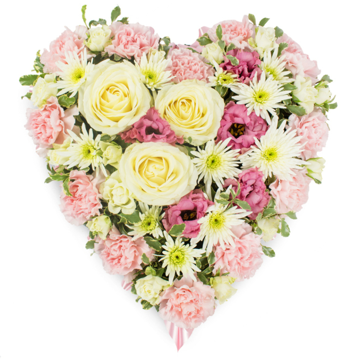 In this detailed image, a lush, heart-shaped funeral wreath is shown against a bright white background, allowing every flower and texture to be easily imagined, as if you were standing in a quiet room near Brent Cross admiring it in person. The heart is thoroughly filled with blooms so that no gaps are visible, only a continuous tapestry of petals in soft pinks, creamy whites, pale yellows, and deeper magenta accents, set off by subtle greenery. At its centre, large roses in shades of cream and buttery yellow unfurl in tightly swirled spirals, their generous, velvety petals suggesting tenderness, gratitude, and a deep, abiding love. Supporting and encircling these focal roses is a dense layer of pastel pink carnations, their frilled, multi-petalled heads forming the main structure and contour of the heart, giving it a soft, cushioned look that feels comforting to the eye. Interwoven amongst the carnations are white spider chrysanthemums, instantly recognisable by their long, narrow petals that fan out from vivid green centres, providing sparkling contrast and a touch of intricate detail. Deeper magenta-pink lisianthus blossoms are scattered thoughtfully throughout, their gently ruffled, bell-shaped flowers enriching the colour palette and adding depth and emotion. Tiny buds and sprigs of variegated foliage peek through the mass of blooms, reinforcing a sense of natural freshness, like a garden momentarily gathered into a single, meaningful shape. At the very tip of the heart, a delicate pink ribbon is just visible, hinting that this arrangement is destined to be laid at a graveside, placed in a chapel, or displayed at a remembrance gathering. The overall effect is of a carefully crafted sympathy heart, ideal for families in the Brent Cross area wishing to express affection, loss, and remembrance through flowers.