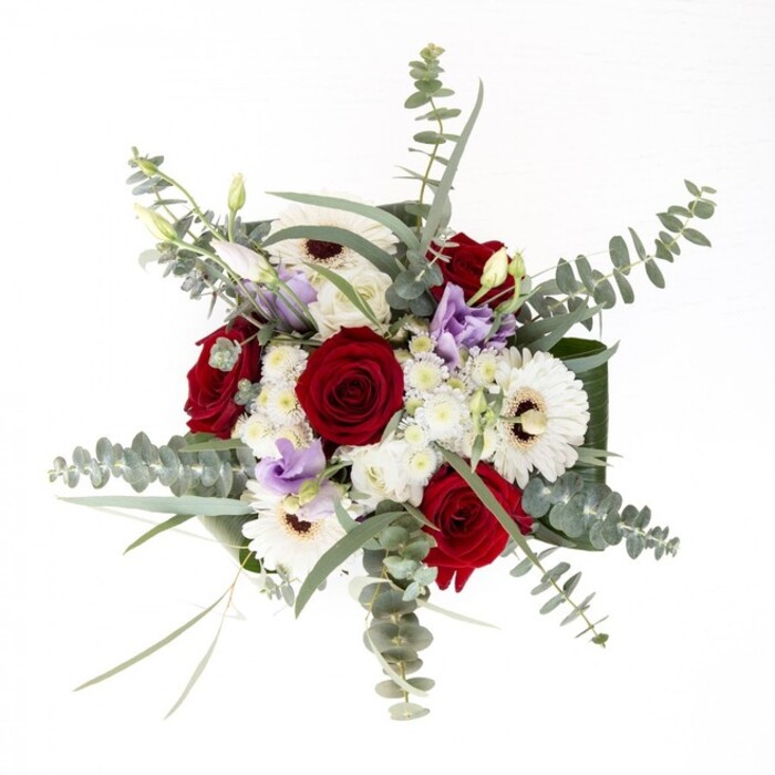 From a florist's perspective in Brent Cross, this bouquet represents the perfect harmony between tradition and fresh design. Large, snowy white gerberas, with their sepia-brown centers, create a serene anchor-mirroring the bright neighbourhood squares on a spring day. Deep red roses, their petals an elegant spiral, signify devotion and passion, surrounded by the whimsical presence of airy, lilac-tinted lisianthus for a contemporary finish. Sprigs of eucalyptus dance above it all, their silvery-green colour recalling the gentle shades of Brent Cross Park; these are paired with fluffy white filler flowers whose texture lends a sense of abundance. At the base, robust, glossy foliage curves elegantly, offering a frame that gives the bouquet both height and grace, while the transparency of the vase showcases the arrangement's freshness with stems visible in the clear water. The bouquet's gentle scent drifts upward, an ever-present blend of eucalyptus and rose, making it just as suited for brightening a new flat in the area as for conveying solace or celebration to friends on a special day. This arrangement channels the authenticity and care Brent Cross Flowers brings to every local doorstep.