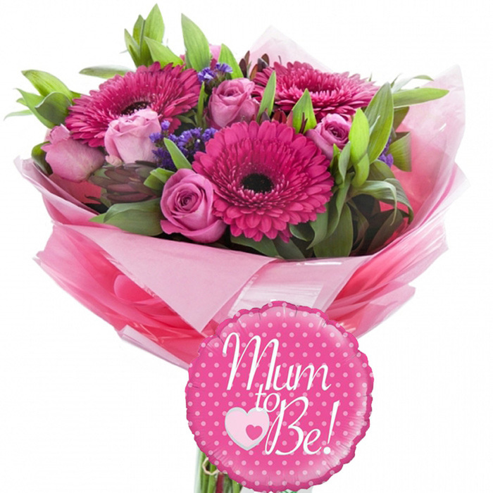 Set against a pristine white background, this joyful Mum to Be bouquet radiates the excitement of a new arrival, much like a bright afternoon around Brent Cross when families gather to celebrate. At the centre of the arrangement, several vibrant fuchsia pink gerbera daisies fan out in perfect circles, their petals smooth and slightly glossy, leading the eye toward deep, dark centres that ground the composition. Threaded harmoniously among them are pastel pink roses, each bloom at a different stage of opening: tight buds hint at forthcoming beauty, while partially opened roses reveal layered petals with a silky, almost velvety texture. Tucked into the spaces between the main flowers, tiny clusters of purple statice or limonium introduce a softer, misty element, breaking up the pink palette with subtle lavender notes and giving the bouquet a textured, multi-dimensional look. The flowers are supported by a generous selection of greenery, including slender bright green leaves and richer, more substantial foliage that curves naturally around the stems, creating a rounded, dome-like silhouette crafted with a florist's practiced hand. The base of the bouquet is wrapped in tiered layers of pink tissue paper-some sheets a gentle blush, others a more vivid candy pink-forming a ruffled collar that feels feminine and celebratory. Over the tissue, a layer of clear, glossy cellophane catches the light, making the colours beneath appear even more vivid, like gift wrap freshly smoothed on a counter at Brent Cross Flowers. Resting prominently at the front, a small round foil balloon in hot pink, edged in a scalloped outline and sprinkled with white polka dots, bears the message Mum to Be! in flowing white script. A sweet dual-heart motif, with a pale pink outline embracing a smaller white heart, sits beneath the words, echoing the theme of mother and child. The overall effect is one of warmth, joy, and anticipation, perfect for a baby shower gathering, a hospital delivery, or a heartfelt surprise for an expectant mum living near Hendon or Golders Green.