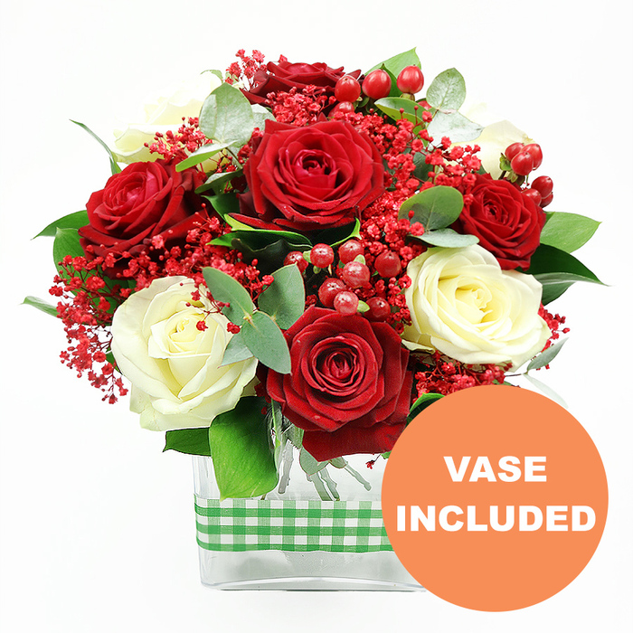 Set against a pristine white background, this lush bouquet of red and white roses appears almost to glow, as if catching gentle daylight filtering through a Brent Cross apartment window. Full-bodied deep red roses, with petals like rich velvet, are interwoven with creamy white roses, whose softly spiralling centers create a romantic, timeless feel. Each blossom is open enough to show its sumptuous structure yet still fresh and tight at the heart, suggesting that the flowers have been arranged recently and are ready for delivery to homes and offices around Brent Cross and nearby Temple Fortune. Threaded among the larger rose heads are delicate sprays of tiny bright red filler flowers, similar to dyed gypsophila; these fine clusters form a feathery layer that softens the contours of the bouquet and adds a sense of lightness and movement. Glossy red hypericum berries pop up at intervals, their rounded forms catching the light like polished gems, giving the design depth and a subtly festive character that makes it suitable for seasonal gatherings, romantic occasions, or milestone celebrations. Supporting and framing the blooms is an assortment of fresh greenery, including slender eucalyptus sprigs with their cool blue-green tint and other foliage in deeper greens. This foliage introduces varied shapes and tones, guiding the eye from the blooms downwards. The stems are gathered neatly in a clear rectangular glass vase, its simple, modern shape allowing the flowers to be the main focus while also revealing the clean-cut, carefully arranged stems within. A green and white gingham ribbon encircles the vase at its midpoint, adding a cosy, rustic accent that would look perfectly at home on a family dining table in Brent Cross. In the lower right corner of the image, an orange circular badge with sharp white lettering declares VASE INCLUDED, signalling that this arrangement is a complete, ready-to-display floral gift ideal for anniversaries, Valentine's Day gestures, or spontaneous expressions of love and gratitude.