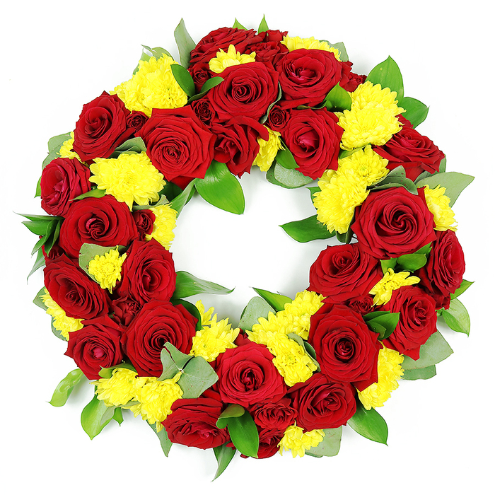 This image shows a beautifully composed circular funeral wreath, photographed in a bright, minimal studio setting so that every flower and leaf stands sharply against a white background. The wreath forms a perfect ring with an empty centre, the floral band made dense and full by an abundance of deep red roses and sunny yellow chrysanthemums placed tightly together. The roses are the focal point, generously scattered throughout the circle. Each rose is at its prime, fully open with velvety petals that spiral outward in neat layers, some petals catching the light on their curved surfaces. Their rich red tone shifts gently from vivid crimson near the heart of the bloom to darker, shaded burgundy along the edges, creating a sense of elegance and depth. Between the roses, numerous clusters of yellow chrysanthemums are woven, their rounded heads composed of many thin petals that produce a textured, almost plush appearance. The yellow colour feels bright yet gentle, a reminder of shared memories and small moments of joy, perhaps echoing family walks through the nearby parks and residential streets of Brent Cross after a service. The floral display is underpinned by a base of varied green foliage. Broad, sturdy leaves with a strong, rich green hue provide the main structure, while shorter stems of muted, grey-green foliage-suggestive of eucalyptus-accent the arrangement with cooler tones and soft edges. The greenery peeks through between the blooms, giving depth without interrupting the wreath's clean circular line. The uniform lighting emphasizes every detail, from fine petal edges to the subtle sheen on the leaves, resulting in an arrangement that appears both carefully planned and naturally abundant. It reads as a thoughtful tribute that Brent Cross Flowers might create for families seeking a refined, respectful floral expression of sympathy and enduring love.