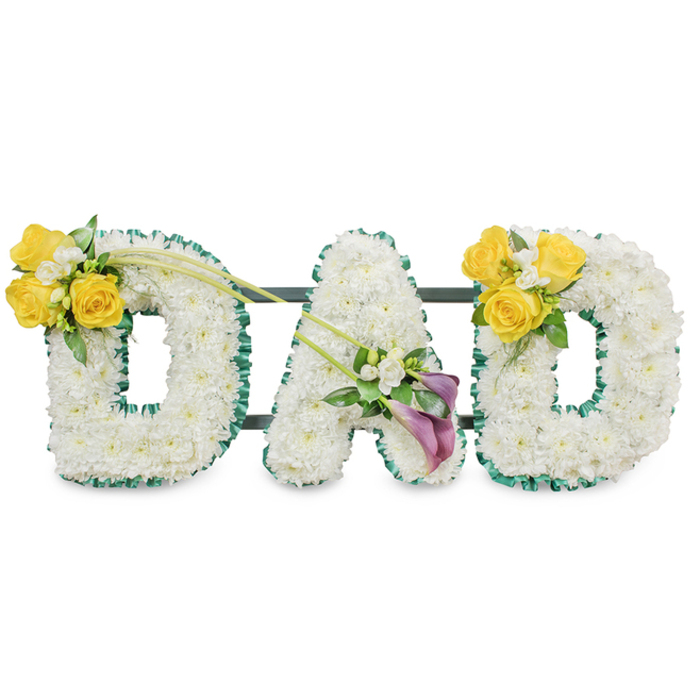A solemn yet tender memorial arrangement composed as the word DAD in three freestanding capital letters, each letter composed from a dense, uniform bed of pristine white spray chrysanthemums that read as soft, cloud-like surfaces under soft studio lighting. The edges of the letters are sharply defined with a ruffled deep green satin ribbon, or narrow foliage, which provides a refined contrast to the white flowers; slim dark green metal support bars run horizontally behind the letters, subtly visible and reinforcing the cohesive structure. On the left-hand 'D' a prominent cluster of bright yellow roses-several in bloom-is placed on the upper curve, accompanied by tiny white filler blooms such as freesias or gypsophila and polished green leaves; two long, bare green stems reach diagonally across toward the centre, creating a gentle line that connects to the middle letter. The central 'A' is adorned low on its left stroke with an elegant grouping of two deep purple or burgundy calla lilies, their sculptural shapes providing a dignified focal point, surrounded by small white accents and soft greenery. The right-hand 'D' mirrors the left with a matching yellow rose cluster on its upper right curve. Set against a plain white background, this arrangement conveys purity, remembrance and quiet respect-a carefully composed funeral tribute suited for services or wakes in Brent Cross and neighbouring communities such as Staples Corner, Cricklewood and Hendon.