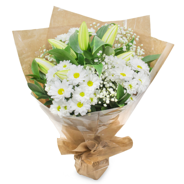 Against a pure white backdrop that removes all distractions, this white and green bouquet is presented as a study in gentle contrast and quiet elegance. At its core is a cushion of daisy-like white chrysanthemums, their petals fine and numerous, placed so closely together they almost overlap. Each flower's centre is a fresh lemon-and-lime shade of yellow-green, adding a subtle, lively spark to the otherwise calm palette. The daisies are arranged to give a softly rounded silhouette, evoking the comfort of a downy pillow or a small, glowing halo. Interwoven amongst these blooms are several closed lily buds, standing a little taller, their long, sleek forms encased in pale green that fades towards creamy white at the tips. Their poised stillness suggests a later moment when the petals will unfurl, bringing fragrance and a new dimension to the arrangement. Throughout the bouquet, delicate stems of gypsophila, or baby's breath, weave in and out, their tiny white flowers suspended like droplets of mist, adding an ethereal lightness that softens the bouquet's outlines. Surrounding the flowers, glossy dark green foliage gently frames the arrangement, with leaves that curve and splay outward to support and showcase the blooms. The stems are neatly bundled and wrapped in a collar of brown kraft paper, its natural, slightly crumpled texture adding warmth and a handmade feel, as though picked up from a favourite florist near Brent Cross station. A final layer of clear cellophane wraps around the paper, reflecting small highlights and ensuring the bouquet is ready for delivery to a family home in Brent Cross, Temple Fortune, or nearby Cricklewood. The overall effect is one of purity, peace, and enduring grace, making it a fitting choice for sympathy, remembrance, or offering quiet strength to someone in need.