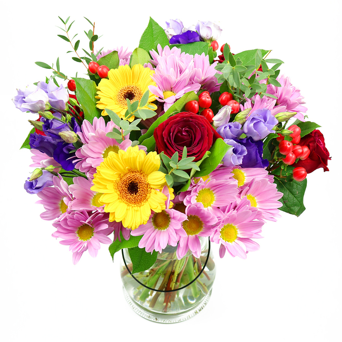 Set against a clean white background, this abundant bouquet in a clear glass vase showcases a harmonious blend of colour and texture that feels both fresh and inviting. Deep red roses sit at the core, their velvety petals layered in tight, luxurious spirals that draw the eye inward and suggest messages of love, gratitude, or admiration often exchanged between families in Brent Cross. Just beside them, two brilliant yellow gerbera daisies with warm, brown-orange centres beam outward, their broad, even petals giving the arrangement an unmistakably joyful expression. Surrounding these focal blooms, a ring of soft pink daisy-style chrysanthemums expands the silhouette; their numerous slender petals and tiny yellow centres create a feathery, cushion-like effect that softens the overall look. Woven throughout the bouquet are graceful stems of lisianthus in tones of purple and lavender, some flowers appearing as gently cupped bells, others fuller and more open with slightly frilled edges, bringing cool, elegant contrast to the warmer hues. Nestled between blooms, small sprays of glossy red hypericum berries offer pops of colour and a rounded, tactile texture, echoing the decorative berries found in well-tended front gardens around Brent Cross. The varied greenery - strong, dark leaves paired with lighter, more delicate sprigs - frames the blooms, lending natural movement and a sense of garden freshness. Through the transparent vase, neatly cut stems stand in clear water, revealing the structure and care beneath the lush top. The bouquet's atmosphere is uplifting yet composed, perfectly suited to marking a birthday, saying thank you, or brightening a living room after a day of shopping along nearby High Road, a stylish but approachable floral accent for everyday celebrations.