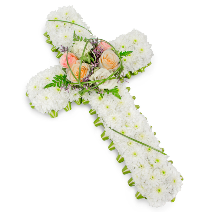 A beautifully arranged floral cross, designed as a funeral or memorial tribute, appears against a pure white background that accentuates its thoughtful composition. The entire shape of the cross is carpeted with pristine white chrysanthemums, their small, rounded heads densely packed so that the surface looks like a soft, textured cushion of petals. The overall feel is one of purity, stillness, and gentle farewell. Running neatly along the entire border is a narrow band of vivid green foliage, clearly defining the cross's outline and framing the white flowers with a crisp, natural edge. This contrast between white and green mirrors the peaceful balance of built streets and open green spaces around Brent Cross. At the central crossing point, a raised spray of larger blooms becomes the emotional heart of the design. Several luxurious roses in shades of soft peach, warm apricot, and creamy ivory stand proudly among the white chrysanthemum base, their petals unfolding in generous layers that suggest tenderness and care. These roses are nestled amidst feathery ferns, rich green leaves, and elegant bows of slender, bright green grass that loop outward, adding rhythm and grace. Tucked within the greenery are dainty purple or lavender filler flowers, introducing small sparks of colour and depth while preserving the overall tranquility. The cross is displayed slightly on the diagonal, encouraging the eye to travel along its length and appreciate the craftsmanship involved. Created with the same attention to detail that Brent Cross Flowers brings to local services, this piece is ideal for a church farewell, crematorium ceremony, or burial ground, expressing faith, love, and a quietly powerful sense of remembrance.