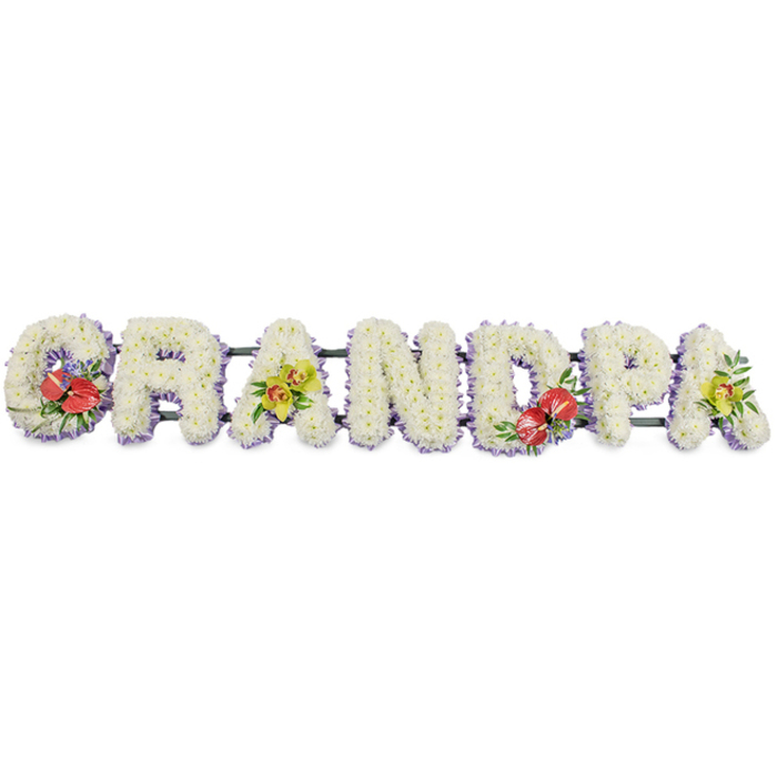 A carefully crafted sympathy arrangement spells out GRANDPA in one continuous line, placed against a bright white background that emphasises every detail. Each letter is made entirely from dense clusters of white chrysanthemum heads, the blooms arranged so closely that they form a thick, cushioned surface like soft fabric. The petals create a gentle, textured pattern, often chosen for funeral tributes to symbolise innocence, peace, and a loving farewell. Along the lower edge of each letter runs a narrow band of light purple ribbon, subtly visible beneath the flowers; this lavender trim provides a delicate frame, separating the letters from the background and adding a quiet touch of colour. Dark green bars support the letters from behind, joining them into a single, horizontal tribute suitable for display at a funeral service, cremation, or graveside ceremony in and around Brent Cross.   

Carefully selected accent flowers personalise the design. On the 'G' at the far left and the 'D' near the centre, bold clusters of deep red anthuriums draw the eye, their heart-shaped, glossy spathes and prominent yellow spadices surrounded by rich green leaves and tiny highlights of purple filler blooms. These passionate red flourishes feel like strong, enduring memories. The first and final 'A' are enriched with sprays of yellow-green orchids, their delicate, arching petals, and intricate centres resting among fresh greenery, bringing elegance and a hint of modern style. The overall impression is of a respectful, heartfelt GRANDPA tribute that a family from Brent Cross might choose to honour a much-loved grandfather, offering a dignified floral message of love, remembrance, and thanks.