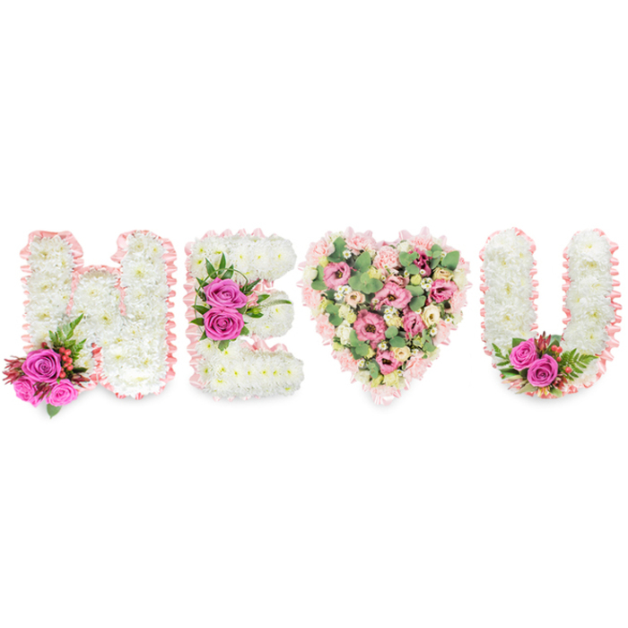 This carefully composed arrangement reads across a clean white plane as H, E, a full heart, and U, a floral sentence shaped to convey devotion, memory, or comfort. The three letters are engineered from tight, snow-white chrysanthemums that give each character a soft, pillowed texture; a delicate blush-pink satin ribbon outlines every edge, its whisper of sheen unifying the set and suggesting a cherished keepsake. The leftmost H is brightened at its base by two bold fuchsia roses, dotted with tiny clusters of reddish berries and framed by fine, fern-like foliage in deep green - a concentrated accent that gives warmth to the otherwise serene palette. The E mirrors the craftsmanship, with a prominent trio of fuchsia roses planted along the central bar to create a visual heartbeat. Between the letters the heart blooms in gentler tones: an abundant mix of pale pink carnations, some spray varieties for texture, and soft lisianthus or small roses, interspersed with muted green eucalyptus that lends a subtle citrus-herbal scent and delicate structure. The U completes the message, echoing the white chrysanthemums and blush ribbon, and carries a small pairing of fuchsia roses nestled into its inner curve to balance the composition. Lit by soft, neutral studio lighting, the display feels intimate and refined - equally appropriate as a celebration of life piece or a romantic statement. Local families across Brent Cross, Cricklewood and Golders Green frequently ask for this kind of personalised wording when they want a floral tribute that speaks plainly and lovingly from the heart.