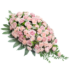 This image shows a beautifully crafted sympathy spray resting on a pure white backdrop, allowing the gentle colours and textures to stand out clearly. The arrangement forms an elegant teardrop, its upper left portion rounded and opulent with flowers, then gradually narrowing into a refined point as it stretches diagonally down to the lower right. The tribute is composed mainly of blush and light peach-pink roses, tightly grouped for a lush effect. Some of the roses are fully open, revealing spirals of soft petals, while others are partially closed, giving the design a sense of depth and quiet movement. Nestled between these are layers of pastel carnations, their ruffled faces adding richness and a slightly feathery texture that contrasts with the smoothness of the rose petals. Dark green foliage frames and anchors the spray. Broad, glossy leaves form the structural base, while lighter, more slender greenery peeks through and trails delicately from the edges, particularly at the pointed end, where fine stems seem to drift like a soft sigh. The palette of muted pinks and greens creates a feeling of serenity, empathy, and warmth. One can imagine this arrangement prepared by a skilled florist near Brent Cross Shopping Centre, ready for same-day delivery to a funeral service in surrounding areas such as Golders Green or Cricklewood. Designed to lie flat, it would rest gracefully on a coffin or memorial table, its softly rounded top drawing the eye while the tapering tail gently leads it away, as though guiding a final farewell. The spray captures both artistry and emotion, offering a tender tribute to a cherished life.