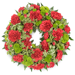 A lush, traditional funeral wreath is presented against a plain white background, giving full focus to its vibrant red and green palette. The wreath's circular form is densely packed, creating an unbroken ring of flowers and foliage symbolising continuity and eternal remembrance. At its heart are numerous red carnations, their petals fluttering in fine, frilled layers that build into generous, full blooms. The red is deep and resonant, neither too bright nor too dark, evoking warmth, love, and respect. Interspersed between these carnations are lively lime green button chrysanthemums, their neat, domed heads composed of countless tiny, velvety florets. The green flowers appear like bright beads woven through the crimson, adding a touch of youthful brightness without diminishing the solemn purpose of the piece. Beneath and around the blooms, dark green ferns and assorted foliage create a rich, textural base, giving the wreath a three-dimensional feel that suggests it might almost lift off the white surface. Variegated leaves with creamy edges add a hint of lightness, reminiscent of the varied foliage you might notice in the landscaped areas surrounding Brent Cross shopping centre and the quiet streets beyond. A green striped ribbon, folded into soft loops, is tucked in among the lower flowers, its subtle pattern echoing the rhythm of the leaves. The overall impression is of a carefully considered design, crafted by an experienced Brent Cross florist for delivery to local churches, crematoria, or family homes. It feels both respectful and gently uplifting, offering comfort and a vivid tribute to a life remembered with love.