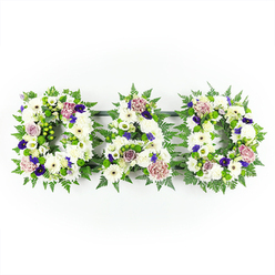 In this image, the word DAD is written not in ink but in flowers, each capital letter built as a full floral arrangement and lined up horizontally against a pristine white background. The letters are generously filled with pure white chrysanthemums and daisy-like blooms, their layered petals overlapping in soft waves to create a thick, comforting blanket of texture. Here and there, smaller white blossoms and buds nestle between the larger heads, reinforcing the sense of abundance and care. Tracing the outside of each D and the central A is a halo of fresh green foliage-light, feathery fern fronds and other leafy stems-that give the tribute clear definition and a gentle, organic outline, reminiscent of the greenery along the pathways and residential gardens around Brent Cross. Punctuating the white canvas are thoughtful touches of colour: deep violet and plum-toned flowers tuck discreetly among the blooms, suggesting dignity and quiet strength, while muted lavender and lilac roses add softness and emotional depth, like memories that feel both tender and bittersweet. The lighting is even and bright, so every detail of petal and leaf is visible and the whites remain clean rather than stark, lending the whole composition a sense of calm clarity. This DAD letter tribute looks like it has been prepared with great attention for a funeral or memorial service in the Brent Cross area, perhaps to rest on the coffin, accompany the hearse, or sit beside a photograph, offering a deeply personal message of love, respect, and remembrance through the language of flowers.