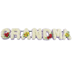 This image captures a classic GRANDMA funeral tribute set against a bright white background, allowing each letter and bloom to be clearly distinguished. The word unfolds across the frame in sturdy block capitals, every letter formed from a thick carpet of tightly clustered white chrysanthemums, their small, ruffled heads creating a soft, pillow-like effect. Just peeping from beneath the white surface is a slender trim of pale lavender or light purple flowers, which traces each letter's outline and lends a subtle, refined glow rather than strong colour. On the leftmost G, three deep red roses sit along the lower left curve, their velvety petals and dark green leaves sending a visual message of enduring love. The first A is decorated with two yellow-green orchid blossoms across its crossbar, each bloom showing a delicate reddish-brown pattern at its centre, adding a hint of exotic grace and individuality. The middle letters R, N, and D are kept intentionally simple, their clean white faces and barely visible lavender edging conveying calm, respect, and purity. Near the right end of the word, the M carries another grouping of three red roses in its lower right section, echoing the affection displayed on the G, while the final A repeats the motif of two lime-tinted orchids, closing the tribute in a gentle symmetry of colour. All the letters are mounted securely to a slim metal frame that runs along the back, making the piece suitable for funeral processions and services across Brent Cross and neighbouring areas such as Cricklewood and Finchley. Crafted in the style of an experienced local florist, the design balances tenderness and tradition, offering a meaningful farewell to a beloved grandmother.
