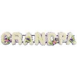 This image shows a lovingly arranged floral name tribute that spells GRANDPA in large, three-dimensional letters, crafted with the steady care of an experienced North London florist. Each of the seven capital letters is generously padded with tight clusters of white chrysanthemums, their small, many-petalled heads forming a smooth, cushioned surface that looks both soft and strong, much like the dependable presence many families remember in a grandfather. Around the edge of every letter runs a neat, continuous edging of small purple and lilac flowers, giving each shape a clear outline and a gentle wash of colour that would stand out gracefully in a Brent Cross chapel or synagogue. Within certain letters, accent sprays add depth and emotion: the G and first A feature elegant lily-like white blooms rising from a bed of pink and fuchsia tones, while the D and second A echo those colours with touches of deep purple and fresh green button chrysanthemums, recalling the lively mix of hues often seen in gardens around Hendon Way and Clitterhouse Playing Fields. All the letters rest on a slender, dark green bar that runs horizontally behind them, quietly holding the tribute in a straight, secure line so it can be placed at the front of a service or beside a coffin. The background is completely white, and the lighting is even and soft, highlighting the freshness of the petals and the detailed workmanship without any distractions. The overall feeling is one of heartfelt respect and gentle comfort, a floral embrace that silently says thank you and we love you to a much-loved grandad, suitable for funeral flower delivery across Brent Cross and neighbouring areas.