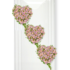 Against a luminous white background, three heart-shaped floral tributes descend in a tender diagonal, creating a visually striking yet quietly comforting funeral arrangement. Each heart is completely filled with roses, their petals layered tightly together in shades of dusty lavender, soft mauve, and gentle pastel pink. The blossoms vary in size and openness, with petite buds nestled among fuller blooms, giving the hearts a sense of depth and life, as though they have just been carefully arranged by a skilled florist in Brent Cross. The colour palette is restrained and elegant, ideal for conveying affection and respect without overwhelming the eye. Carefully threaded through the design, strands of fresh ivy trace the outline of each heart, their rich green leaves providing a graceful contrast to the cool, powdery tones of the roses. These vines then stretch between the hearts, forming natural bridges that symbolise connection, continuity, and the ties that hold families together through joy and sorrow. Soft, even lighting falls across the display, enhancing every curve of petal and leaf while creating faint vertical reflections in the background, suggestive of glass panels or a bright, contemporary interior space near Brent Cross Shopping Centre or on the quieter residential streets beyond. The overall impression is one of serenity and sincere emotion, a tribute that could be placed beside a coffin, at a memorial service, or by a photograph of a loved one. It speaks of devotion, shared memories, and the wish to send someone off with a final gesture of beauty and heartfelt care.