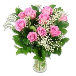 An elegant display of pink roses and white baby's breath rests in a clear glass vase, set against a bright, immaculate white backdrop that allows the colours to glow softly. The bouquet features approximately ten to twelve pink roses, their petals unfolding in layered spirals from delicate, light pink at the outer edges to a more saturated rosy tone toward the centres. Some flowers are in full bloom, revealing their intricate, velvety hearts, while others are still gently cupped, adding a sense of movement and freshness, like a newly arranged gift waiting to be delivered across Brent Cross. Fine, branching stems of baby's breath lace through the arrangement, each carrying numerous tiny white blossoms that form a bridal veil of texture, suggesting purity and innocence often chosen for baby gifts and christening flowers. The roses and filler are framed by dark green foliage, with smooth, firm leaves that add structure and depth, balancing the lightness of the pink and white flowers with a grounded, natural base. The vase itself is transparent and unfussy, filled with clear water that reveals the evenly trimmed green stems inside, reinforcing the impression of recent cutting and expert conditioning by the local florists at Brent Cross Flowers. Bright, even lighting bathes the arrangement, emphasising the gentle sheen on the leaves and the soft, almost satin-like texture of the petals, while the seamless white background keeps the viewer's attention fixed entirely on the blooms. This bouquet conveys warmth, welcome, and gentle happiness, making it a fitting image for stories about new babies, family celebrations, or thoughtful gifts delivered around Brent Cross Shopping Centre and the surrounding residential streets.