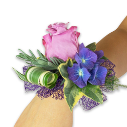A soft, atmospheric corsage sits diagonally on a fair wrist, where botanical artistry and tender romance meet in miniature. The focal rose is a plush mauve-pink bloom, partially open so that its layered petals form a calm, concentric bloom with a subtle sheen that suggests a faint, dewy perfume. To either side, saturated indigo hydrangea clusters offer textural contrast; each tiny floret centers on a pale bluish disc that seems to catch and reflect light, nodding to dusky summer skies. Working around these blooms are silvery-green sprigs-eucalyptus or lavender-like in appearance-that give a soft, whispering backdrop and a lightly aromatic lift. Variegated English ivy, with deep green hearts rimmed in cream, frames the arrangement with a graceful, old-world touch while a wide striped leaf with bold white and green banding is coiled into a modern loop, adding sculptural movement. Underpinning the design is a dark purple, open-mesh ribbon whose airy lace lifts the flowers and adds a gentle shimmer, echoing the hydrangeas' deep tones. The textures are intimately composed: plush rose, papery hydrangea, glossy ivy and polished curled foliage all balanced to invite both sight and touch. The overall effect is quietly celebratory-perfect for bridesmaids, prom escorts, or anyone who wants a refined floral accent. I picture this piece being delivered around Brent Cross, nestled among the shopping centre and nearby boulevards, ready to accompany an evening of memories with a fresh, garden-scented promise.