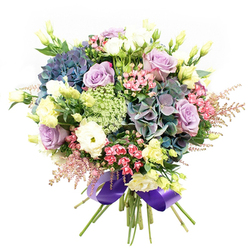 Brent Cross Flowers presents a bouquet that radiates opulence and delicate grace-a carefully crafted arrangement inspired by the energy and greenery surrounding Brent Cross's iconic shopping precinct. At the core are resplendent hydrangeas, their petals awash in rich indigo and teal tones, offering plushness and depth reminiscent of Hendon Park in spring. Nestled between, elegant roses in pastel lavender and pristine ivory unfold, their layers lending a sense of romance and enduring beauty to the composition. White ranunculus, tightly packed and multi-petaled, add textural contrast, while pale yellow eustoma buds emerge with a fresh, airy brightness. Sprays of energetic fuchsia and soft, gossamer-pink astilbe scatter throughout, bringing playful pops of colour and a gentle, whimsical movement to the bouquet's edges. Lacy filler blooms-possibly Ammi Majus or Queen Anne's Lace-thread delicately among the main flowers, enhancing both structure and lightness. Deep, rich foliage provides balance, firmness, and a vibrant backdrop. The stems are meticulously gathered and secured at the base with a luxurious, wide royal purple satin ribbon, echoing the bouquet's cool, sophisticated palette. Timeless and perfectly poised, this arrangement is ideal for birthdays, anniversaries, or elevating everyday moments at home or in local offices, encapsulating the unique charm of Brent Cross with every scent and petal.