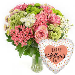 A lush Mother's Day floral gift is captured in a bright, uncluttered image, making every bloom, leaf and reflection stand out. In the centre sits a clear glass vase, filled with clean water and carefully trimmed stems, supporting a rounded bouquet that feels both full and airy. Prominent within the design are large pink roses with gently curving petals, the centres rich and rosy, the outer edges softly fading to paler shades, like a gentle blush. Around the roses, dense clusters of coral-pink flowers-evoking kalanchoe or similar small florets-create texture and warmth, while the occasional spikier coral bloom adds a touch of spirited movement, echoing the swirl of people and traffic around Brent Cross. Lime-green button chrysanthemums and plush, chartreuse, cockscomb-style forms pop from the arrangement, their vivid colour adding an invigorating jolt and their unusual, almost moss-like surfaces making the display visually intriguing. Scattered white spray chrysanthemums, with bright daisy-like faces, introduce pockets of lightness, ensuring the palette remains crisp and uplifting. Fine details, such as tiny pale-tipped chrysanthemum centres and overlapping dark green leaves, reward a closer look, revealing the florist's care and craftsmanship, much like the attention to detail you'd find at Brent Cross Flowers. The bouquet is photographed from slightly above and to the side, showing its domed shape and the pleasant balance of colour. To the right of the vase, a reflective heart-shaped foil balloon brings a festive flourish. Its white background is decorated with irregular, shimmering dots of gold, silver and soft coral-peach, and in the middle a solid peach heart frames the message HAPPY Mother's DAY in elegant black letters. Together, the arrangement and balloon radiate affection and appreciation, ideal for a Mother's Day delivery to homes and apartments across Brent Cross.