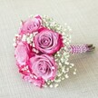 Crafted by florists near Brent Cross Shopping Centre, this vibrant bouquet exudes romance and modern charm. Five large, fuchsia-pink roses unfurl gracefully, revealing soft lavender centers and vivid magenta edges in a harmonious display of colour and texture. Wisps of white baby's breath, delicately interspersed among the roses, lend the arrangement a feathery lightness reminiscent of the gentle winds that sweep over Brent Reservoir. The stems are expertly bound with a deep pink, subtly sparkling ribbon, offering a tactile, refined handle. Parallel strands of lustrous white pearls spiral around the wrapped stems, their gentle glimmer evoking the elegance of Brent Cross wedding celebrations. The bouquet rests casually on a neutral linen surface, echoing the relaxed yet sophisticated style of north London gatherings. Designed with weddings and milestone events in mind, this bouquet symbolises love, joy, and expert floral craftsmanship-a reflection of cherished moments celebrated with friends and family in the Brent Cross community.