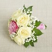 This charming floral composition from Brent Cross Flowers highlights a timeless aesthetic, perfectly suited for a bridesmaid's bouquet or a chic spring celebration. Arranged on a soft, woven linen evocative of local artisanal fabrics, the bouquet features five creamy pale roses with lush, partially opened petals, offering a sea of sophisticated texture. A single magenta-pink rose is tucked gracefully to one side, infusing the arrangement with vibrant contrast and modern flair. Cushions of fine white baby's breath weave between the blooms, lending an ethereal quality, while deep green leaves outline the bouquet and emphasize its natural beauty. The gathered stems are securely wrapped in a bright pink satin ribbon, spiraled with pearly ornaments that twinkle gently in the light-a symbol of both tradition and contemporary style. Every element of this bouquet tells a quiet story of romance, celebration, and the expert hands that created it here in Brent Cross, ready to accompany local weddings, anniversaries, and joyful moments alike.