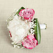 Set against a subtly textured off-white fabric that hints at natural linen, this hand-tied bouquet is captured from a slightly elevated viewpoint, showcasing the thoughtful balance of colour and form. At its heart, a plush creamy white peony unfurls in many layers, each ruffled petal overlapping the next to build a rounded, cloud-like bloom that feels serene and luxurious. Above and below the peony, two vivid pink roses are nestled, their tightly wound centres spiralling outward in graceful curves. The petals blend from a gentle, romantic pink in the middle to richer magenta at the tips, creating a beautiful gradient that adds energy and sophistication, reminiscent of evening lights around Brent Cross. Interlaced between these focal flowers are delicate stems of gypsophila, or baby's breath, each one carrying tiny, soft white blossoms that form a light, airy veil around the larger blooms, giving the bouquet a dreamy and almost weightless quality. At the base, wide, glossy dark green leaves embrace the stems, folding themselves neatly into a smooth, sculpted collar that anchors the design and frames the softness above. The stems are tightly bound with a pristine white satin ribbon, suggesting that this bouquet is intended to be held, perhaps by a bride walking into a ceremony near Brent Cross Shopping Centre or by someone surprising a loved one at home. The neutral background and soft lighting let the creamy whites, bright pinks, and rich greens stand out, conveying a sense of fresh, hand-crafted elegance and the quiet excitement of a special occasion. The image reflects the refined, heartfelt style associated with Brent Cross Flowers and their local wedding creations.