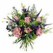 A voluminous, hand-tied bouquet is captured from a slightly overhead angle, standing out vividly against a plain white background and drawing attention to every petal and leaf. At its centre, several pastel pink roses unfold in soft spirals, some still modestly cupped, others fully open so that their layered hearts in deeper blush tones fade outwards to gentle, almost creamy edges. Cradling them are plush carnations in dusty rose and mauve, their densely ruffled petals forming a textured cushion that suggests warmth and romance. Rising through this soft base are elegant stalks of Veronica in deep violet and blue-lavender, their long, tapering flower spikes creating height and movement, not unlike the lines of the flyovers and bridges that define the Brent Cross skyline. Around these vertical elements, clusters of rich purple lisianthus and sprays of tiny, daisy-like aster blooms in pale lavender-blue with small yellow centers add a light, airy quality, evoking the feel of wildflowers gathered from nearby green spaces in Hendon or along the paths by Brent Reservoir. The bouquet is wrapped in generous greenery: bright lime-green filler flowers and chartreuse textures contrast with cool eucalyptus leaves and other foliage in shades of silvery and deep green, framing the blossoms and adding freshness. At the bottom, the neatly aligned stems are clearly visible, bound together in a classic hand-tied style ready to slip into a favourite vase in a home near Brent Cross shopping centre or along the North Circular. The overall impression is one of calm celebration and gentle joy, perfect for sending as a thoughtful gift, a birthday surprise, or a comforting gesture to someone special in NW11.