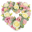 A soft, romantic heart-shaped wreath designed for sympathy and remembrance is displayed against a stark white backdrop, making its pastel flowers appear even more gentle and inviting. The heart is fully formed and generously filled with blooms, creating a feeling of plush, layered petals. Cream and pale yellow roses are the most prominent flowers, their rounded, spiralled heads and silky texture conveying grace and affectionate memories. Weaving carefully around them are clusters of light pink carnations, whose frilled, ruffled petals give the arrangement a delicate, almost whispery texture. To deepen the palette, richer tones of mauve and rosy lisianthus are dotted throughout, their open, trumpet-shaped flowers drawing the eye inward and adding subtle emotional intensity. Cool, silvery-green eucalyptus leaves snake around and between the blooms, tracing the heart's outline and introducing a calming, muted green note, as well as a faint, refreshing scent. Tiny, tightly closed yellow-green buds punctuate the design, suggesting the thread of life continuing on. The colours-creams, blush pinks, gentle yellows, and soft greens-blend into an overall mood of tranquillity and quiet consolation. This heart wreath feels like a thoughtfully crafted tribute from a local Brent Cross florist, perfectly suited for funerals, chapel services, or memorials throughout Brent Cross, Hendon, and neighbouring Barnet. It has the character of a piece chosen by close family or dear friends, an arrangement that sits close to the heart in every sense, offering a floral embrace of sympathy and support during a time of loss.