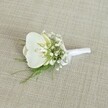 A single white orchid boutonniere rests on a softly textured light beige fabric, its woven surface resembling the natural linen often seen in chic Brent Cross wedding venues. At the heart of the design, a pristine Phalaenopsis orchid bloom opens with calm grace, its broad, velvety white petals slightly glossy in the gentle, even lighting. In the centre of the flower, a hint of pale yellow glows from the throat of the orchid, adding gentle warmth and a touch of depth to the otherwise pure, cool white. Encircling this focal bloom are airy clusters of tiny white baby's breath, their cloud-like sprays softening the orchid's sculptural form and creating a halo of delicate texture. Fine strands of slender, fresh green foliage, similar to asparagus or maidenhair fern, weave through the composition, peeking out from beneath the flowers and giving a whisper of woodland freshness, as if just gathered from a shaded corner of a garden near Brent Cross Park. The stems are neatly aligned and carefully wrapped with a pristine white satin ribbon, the smooth, matte fabric pulled tight and finished in a small, understated bow at the base, ready to be pinned to a lapel. The neutral oatmeal background keeps the focus on the crisp whites and vivid greens, evoking a mood of quiet elegance and modern simplicity. This refined floral accessory feels perfect for a groom or groomsman arriving at a ceremony near the shopping centre or along the Edgware Road, conveying understated sophistication, purity, and the promise of new beginnings with every carefully placed petal and sprig.