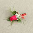 In this image, a single magenta-pink rose forms the elegant centre of a wedding-style boutonnière. The rose itself is perfectly opened, each petal layered gently over the next, with a velvety surface that suggests softness and care. Surrounding the bloom is a compact spray of textured greenery: rich, dark green leaves cradle the base, while fine, reed-like blades of grass rise behind and arc outward, giving the overall arrangement height and a sense of fluid motion, much like the flow of people around Brent Cross station on a busy weekend. Nestled among the foliage are airy clusters of white gypsophila, the miniature flowers appearing almost like a cloud of tiny stars, providing contrast and a classic, romantic touch. The stem has been meticulously wrapped in a shiny red ribbon, the satin material catching the light and adding a bold, festive accent that hints at celebration-perhaps a groom's buttonhole for a ceremony nearby. The backdrop is a neutral, slightly textured fabric that lets the colours of the boutonnière stand out cleanly without distraction. You can imagine holding this piece: the smoothness of the ribbon, the slight spring of the foliage, and the gentle fragrance of the rose rising with each breath. It is a small composition, yet it feels complete and thoughtfully balanced, the kind of handcrafted detail that can transform a suit or jacket into something truly special for a wedding or formal event in and around Brent Cross.