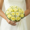A bride clutching this compact bouquet feels immediately wrapped in a gentle sense of peace and warmth. The pale yellow roses-soft as new butter-are set close together so each blossom supports the next, petals forming layered spirals that invite the eye to rest at the centre. Sprays of white baby's breath float above and between the roses like morning mist, their tiny circular blooms creating a delicate, frothy texture that lightens the composition. The bouquet is finished with slender loops of deep green grass and a neat green collar, which give the piece structure and a subtle, contemporary edge while keeping the overall line soft and finished. As a florist who prepares wedding flowers for couples in Brent Cross and the surrounding streets near the shopping centre and Hendon Park, I design this kind of bouquet to sit comfortably in the bride's hands throughout the ceremony: poised, understated and fragrant. You can almost sense the scent-an understated mix of fresh cut greens and the faint honeyed, slightly creamy aroma of the roses-enough to be intimate but not overwhelming. The arrangement is ideal for a ceremony that favours timeless simplicity; it frames the bride's silhouette without competing with gown details and photographs beautifully in natural or diffused church light. For local brides seeking refined romance, this bouquet suggests devotion, tenderness and the kind of careful craftsmanship Brent Cross Flowers is known to deliver across the neighbourhood.
