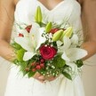 This bridal bouquet, conjured by Brent Cross's local florists, feels as fresh as a dawn in nearby Clitterhouse Playing Fields. Sumptuous white lilies bloom generously, their petals silky and luminous beside the bride's elegant dress. Tucked between, scarlet roses pulse with romantic intent, their softness and scent hinting at stories yet to be written. Playful hypericum berries provide flickers of jubilant red, while clouds of white baby's breath soften the silhouette, mimicking the gentle drizzle of floral confetti. Mossy green globes and fern-like foliage offer a richly textured foundation-natural, wild, and celebratory. Every detail imagines the bouquet hand-gathered from the best of North West London's seasonal bounty, arranged to reflect the bride's joy as she walks the aisle. Balanced and serene, the bouquet is designed to resonate long after the ceremony, its colours, textures, and fragrances lingering in memory just like the northeastern sunlight pouring over Brent Cross on the happiest of days.