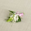 A delicately handcrafted boutonniere lies on a softly textured, light beige fabric that looks like natural linen, the neutral background gently framing every detail of the flowers. At the centre sits a single white alstroemeria, its broad petals opening gracefully to reveal fine reddish-brown speckles near the throat and pale green veins that catch the light. To the left, a tight, conical spike of vivid lime-green buds, reminiscent of Ornithogalum, introduces a striking sculptural contrast, each bud packed closely like tiny scales. Around these focal elements, clouds of dainty white baby's breath weave in and out, their miniature blooms creating a soft, misty halo that lightens the compact design. A foundation of dark green, sword-shaped leaves cradles the flowers, while slender, grass-like fronds arc outward, adding movement and a sense of gentle spontaneity, much like a breeze across Brent Cross's quieter residential streets. At the right side, the stems are neatly gathered and finished with a glossy pink satin ribbon, tied into a small, precise bow that brings a playful, romantic note without overwhelming the calm palette of white and green. The lighting is even and natural, with no harsh shadows, so the textures of petal, leaf, and fabric are all clearly defined: the silky sheen of the ribbon, the smooth firmness of the buds, the slightly ruffled edges of the alstroemeria, and the soft weave of the cloth beneath. The overall impression is of thoughtful, refined craftsmanship-a boutonniere perfect for a wedding, prom, or anniversary celebration in Brent Cross, ready to be pinned to a lapel or fastened to a dress for a day of quiet joy and understated elegance.