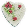 A heart-shaped memorial spray, photographed on a clean white background, made from a densely packed cushion of small, pristine white chrysanthemums that create a cloud-like, textured surface. The chrysanthemums read as soft and matte under a gentle, overhead light that throws faint shadows into the flower heads, giving the heart a quiet depth and a sense of peace. From the upper left a diagonal emphasis of deep crimson roses rises - three roses clustered closely together amid glossy green foliage and delicate, fern-like fronds - their fully unfurled petals offering a warm, solemn red that contrasts the cool white cushion. Two additional red roses punctuate the composition: one nestling near the upper right curve of the heart and a second placed toward the lower point, each with a few small green leaves and subtle looping blades of bear grass that add movement and a handcrafted flourish. Tiny white filler blooms peek through the foliage, and a slim emerald-green satin ribbon traces the heart's outer edge, framing the piece with a refined touch and reinforcing the classic silhouette. The overall effect is one of calm reverence - a traditional sympathy arrangement that reads as both dignified and tender - suited for funeral services, a graveside tribute, or as a comforting visual for articles about bereavement and remembrance. As a florist who knows Brent Cross and nearby Cricklewood, I picture this piece placed beside a funeral program or a small sprig of lavender from a local garden, offering a composed, respectful farewell for a loved one in the community.