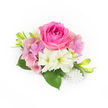 A compact, couture-like corsage rests against a pristine white backdrop, the image lit in soft natural light that highlights texture and colour. At its centre sits a lush bubblegum-fuchsia rose, its tightly furled inner petals opening into a plush bloom whose velvety surface catches a gentle sheen. Encircling the rose are cloud-like clusters of pastel pink and lavender hydrangea florets, their papery petals building a soft, romantic volume that offsets the rose's dense silhouette. Paired beneath and slightly to one side, two creamy white, trumpet-shaped blossoms-small amaryllis or miniature lilies-showcase pale green throats, adding a cool, luminous counterpoint to the warm pinks. Glossy, deep-green leaves form a verdant cradle, their broad surfaces grounding the composition while slender, bright green buds tipped with yellow climb upward, suggesting future opening and freshness. A tasteful cascade of small, lustrous white pearls spills at the lower right, varying slightly in size to lend a vintage, heirloom accent that reads immediately as bridal or formal. The arrangement smells faintly of garden roses and early-morning dew, a quiet scent evoking spring evenings and carefully chosen details. Created with the careful hand of a local florist familiar with Brent Cross sensibilities, this piece suits weddings, proms, and intimate anniversary moments-an accessory that reads both refined and sincere. The overall balance of colour, light, and texture makes it ideal as a bridal corsage or refined gift for a celebration in the Brent Cross neighbourhood, where classic taste meets modern simplicity.