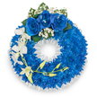 A vibrant, meticulously constructed circular wreath sits against a bright white backdrop, its design immediately defined by a dense, plush ring of vivid electric-blue chrysanthemums that create a velvet-like texture across the whole form. The blue blooms are packed closely, petal against petal, so the circle reads as a saturated, luminous field of colour. Crowning the top are three large royal blue roses, their velvety petals unfurled in full bloom and gently nestling against tiny clusters of white baby's breath, which soften the intensity with feathery halos of white. Deep green leaves peek through the roses, adding a quiet, natural contrast.

From the left side a graceful spray of pristine white orchids-likely Phalaenopsis with broad, open petals-cascades downwards, introducing slender lines that break the wreath's circular geometry and convey movement and delicate resilience. A slender, curving stem studded with pale yellow-green buds threads among the orchids, hinting at new life and unfolding beauty. The wreath's inner edge is neatly finished with a ruffled white satin ribbon, its crisp sheen framing the central opening and lending a formal, respectful edge. Soft, clean lighting highlights the electric blues and the satin sheen, while a subtle floral scent of chrysanthemum and orchid suggests a quiet, contemplative atmosphere. This arrangement carries the language of remembrance-serene blues, pure whites, and considered textures-suitable for a funeral or memorial service and crafted with the careful attention of a local Brent Cross florist familiar with the neighbourhood's needs for dignity and comfort.